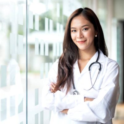 Smiling Asian female doctor in lab coat with arms crossed against looking at camera.